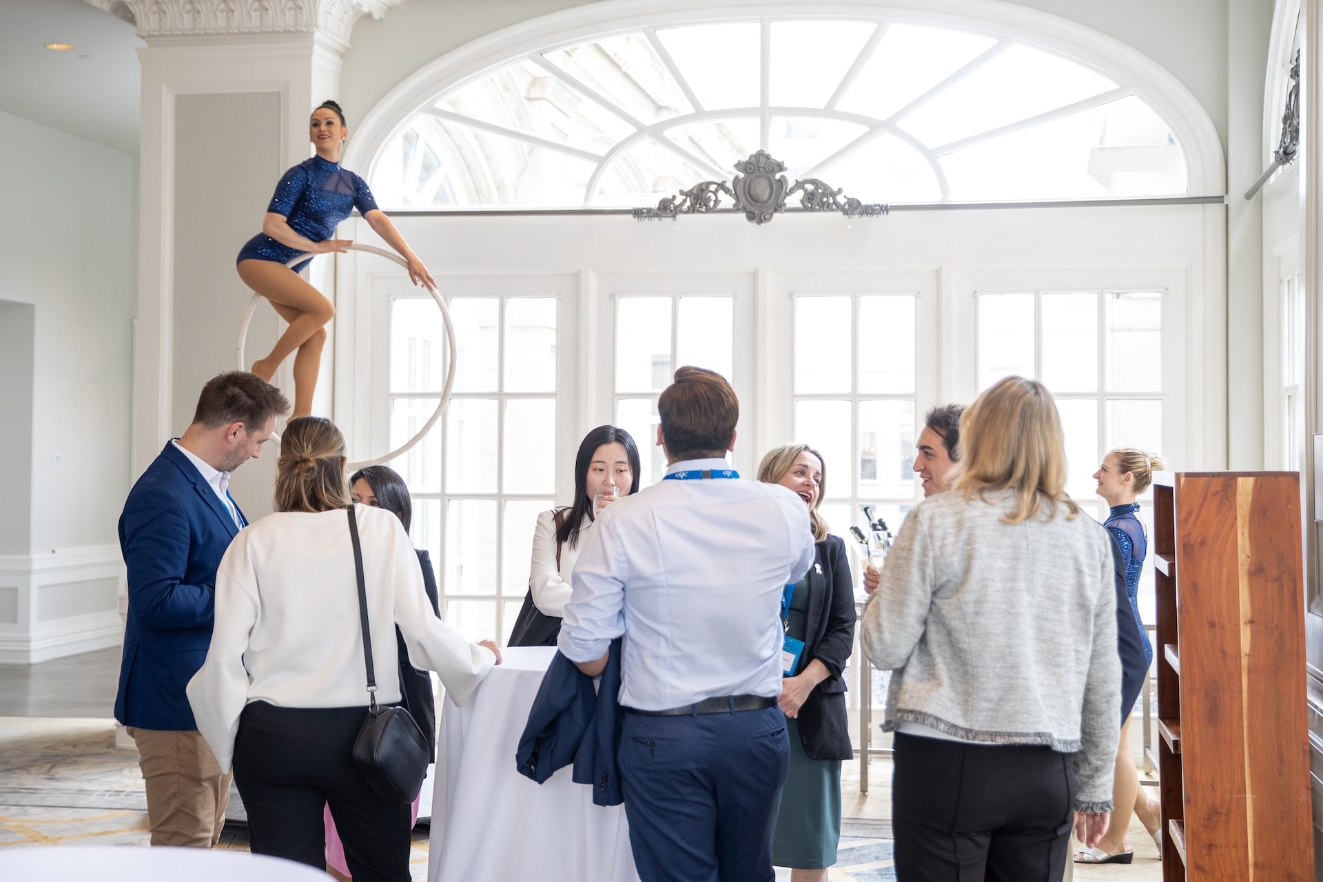 A performer on an aerial hoop above a group of people engaged in conversation at a social event.